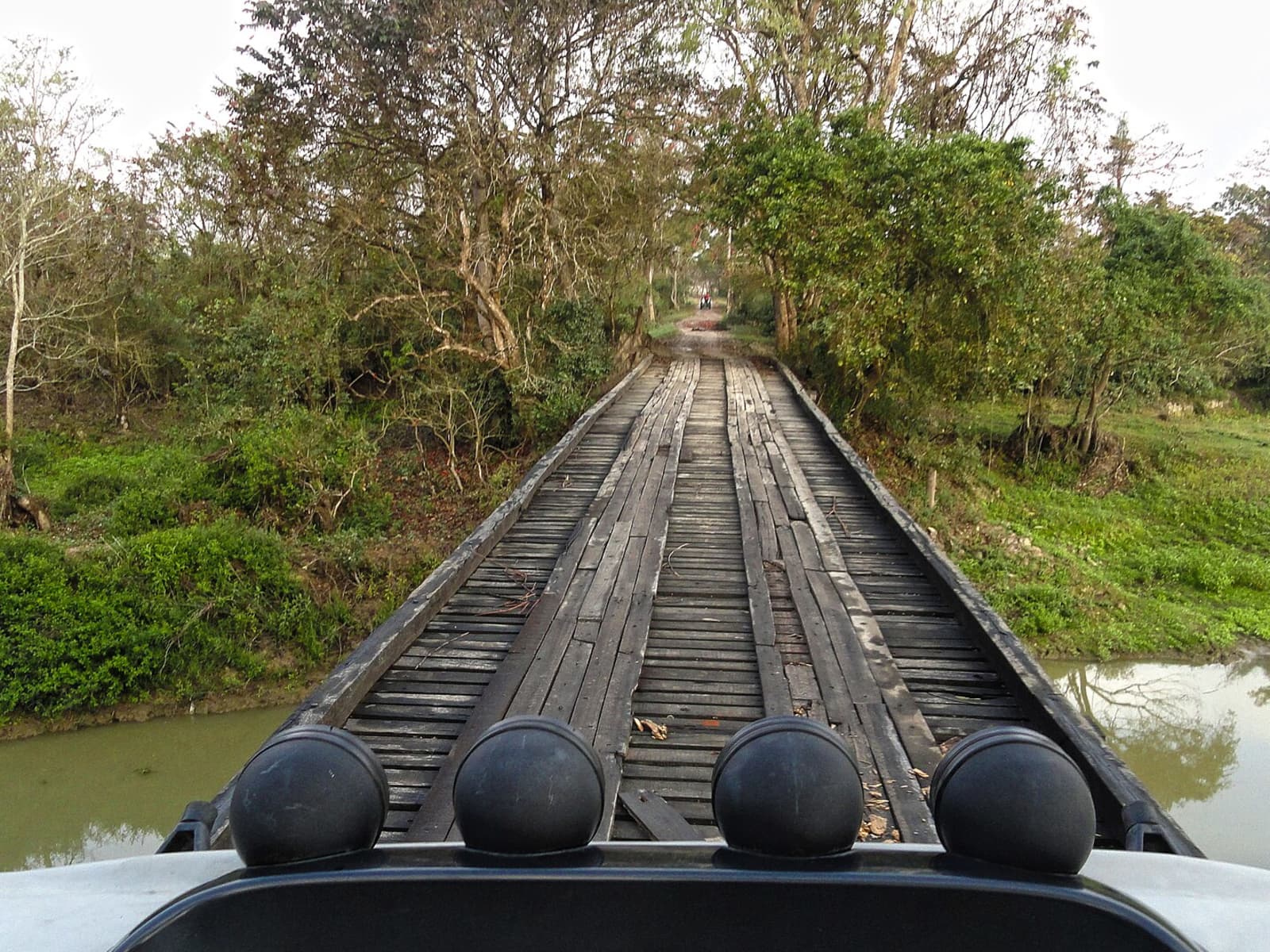 Jeep safari vehicle driving onto a rustic wooden timber bridge spanning a forest stream inside Burapahar.