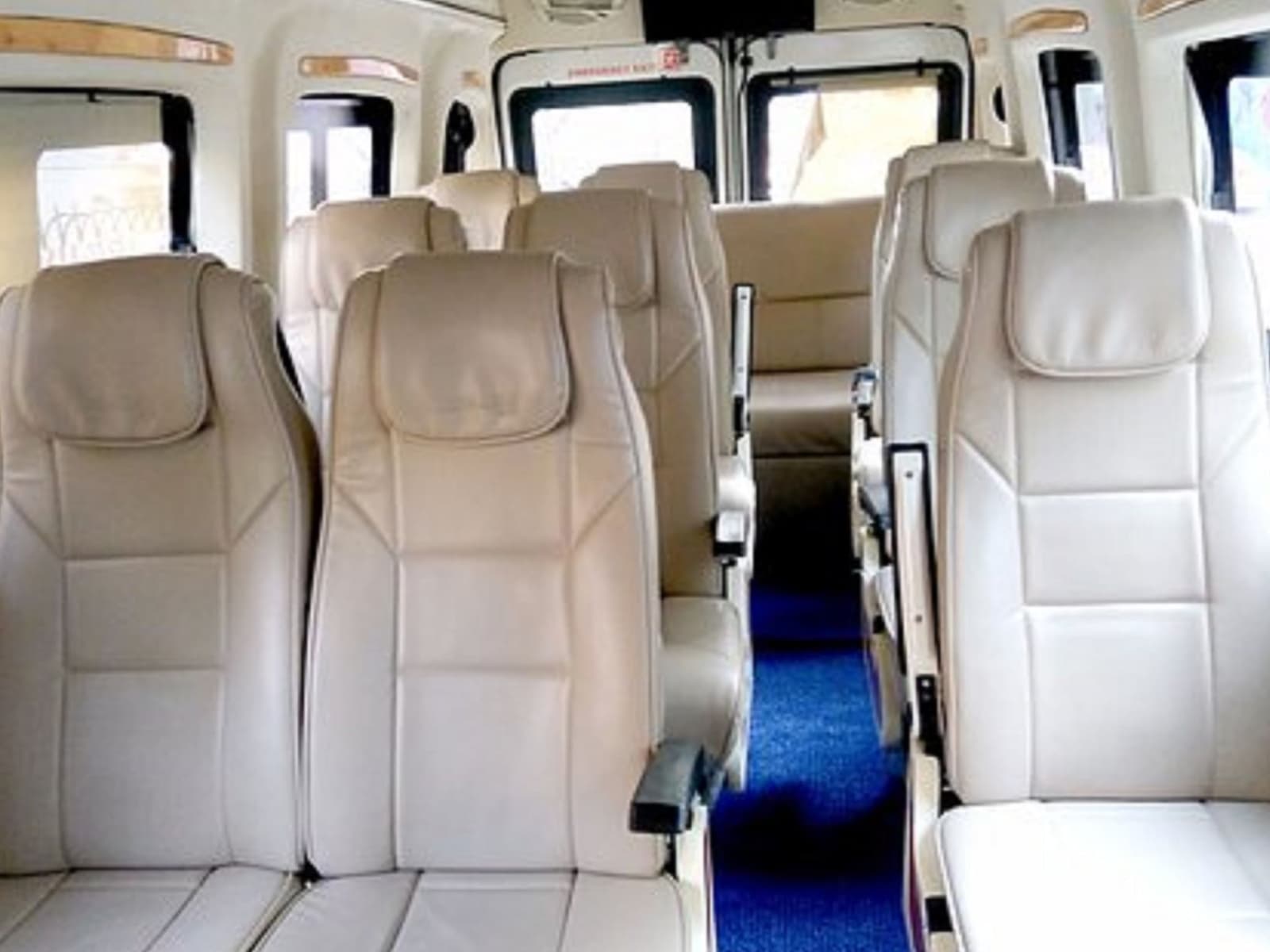 Force Tempo Traveller luxury cabin featuring individual beige leather pushback reclining seats, armrests, and central carpeted aisle.