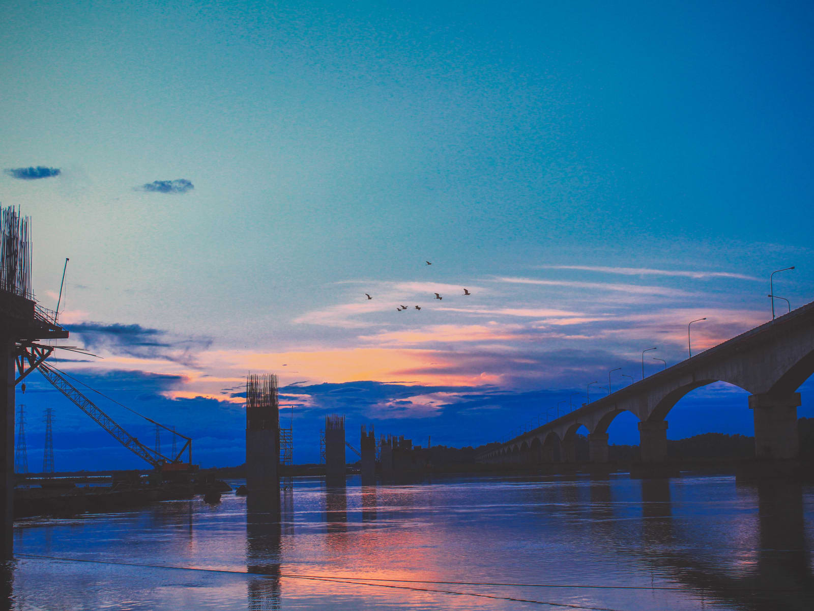 Kolia Bhomora Setu spans the wide Brahmaputra River during golden hour sunset with water reflections.