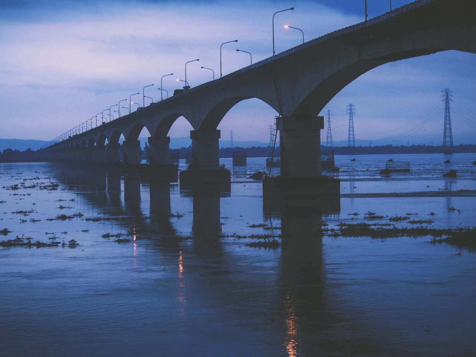 Concrete piers of Kolia Bhomora Setu stand across the Brahmaputra River under a soft purple twilight sky.