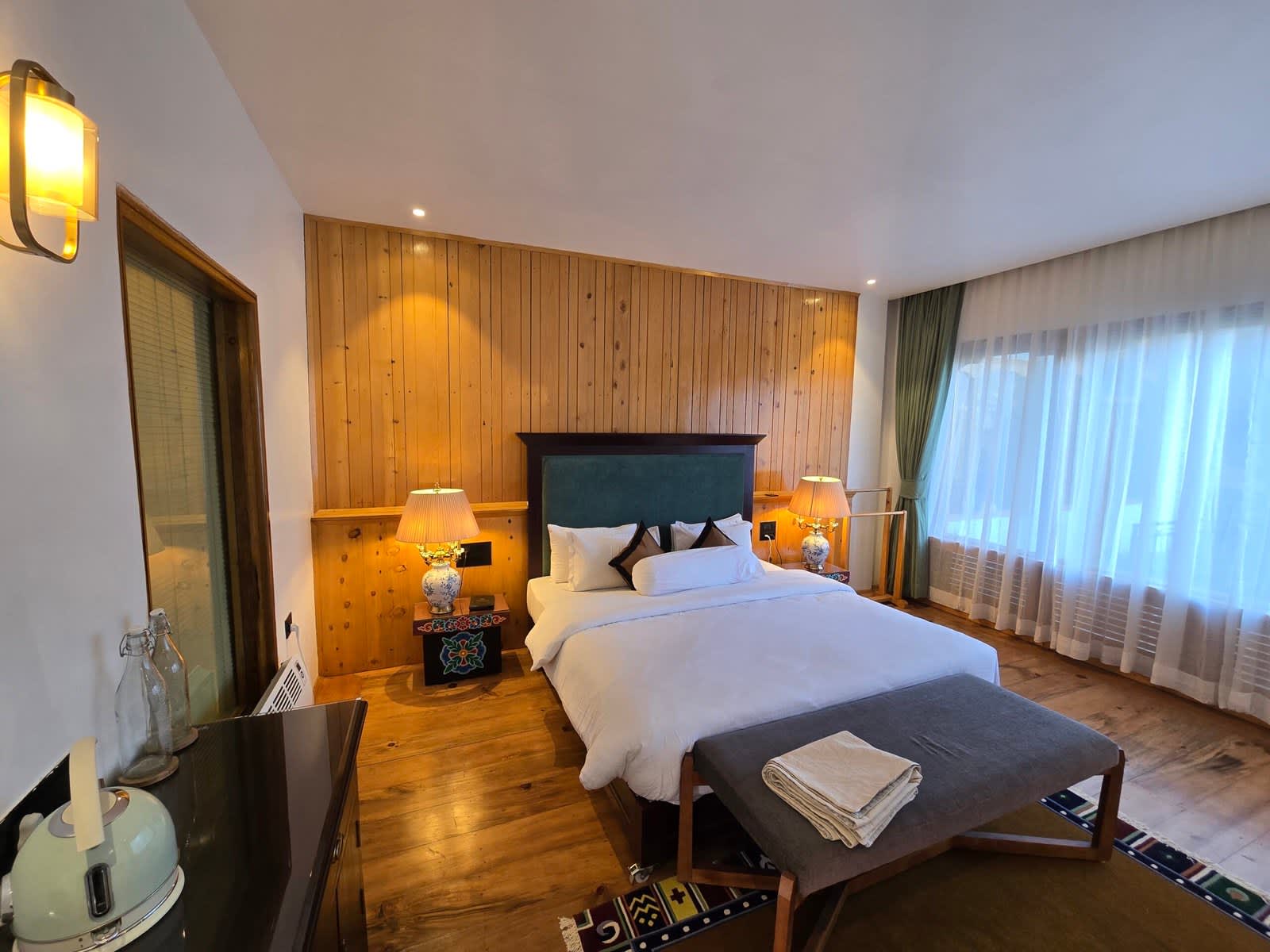 Warm lamps illuminate white linens beside traditional pine wall slats.