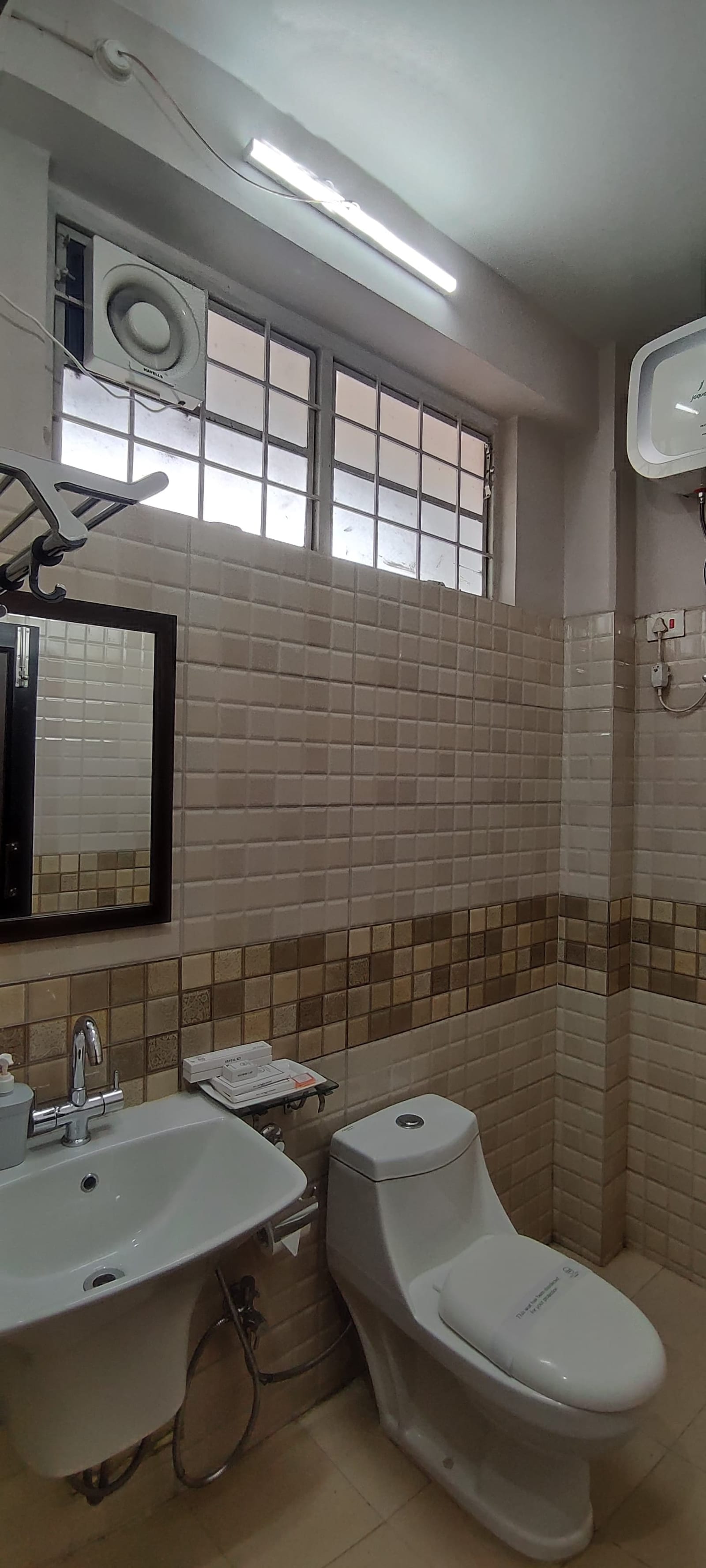 Modern ensuite bathroom featuring ceramic wall tiles, chrome sink fixtures, vanity mirror, and ceiling exhaust fan.