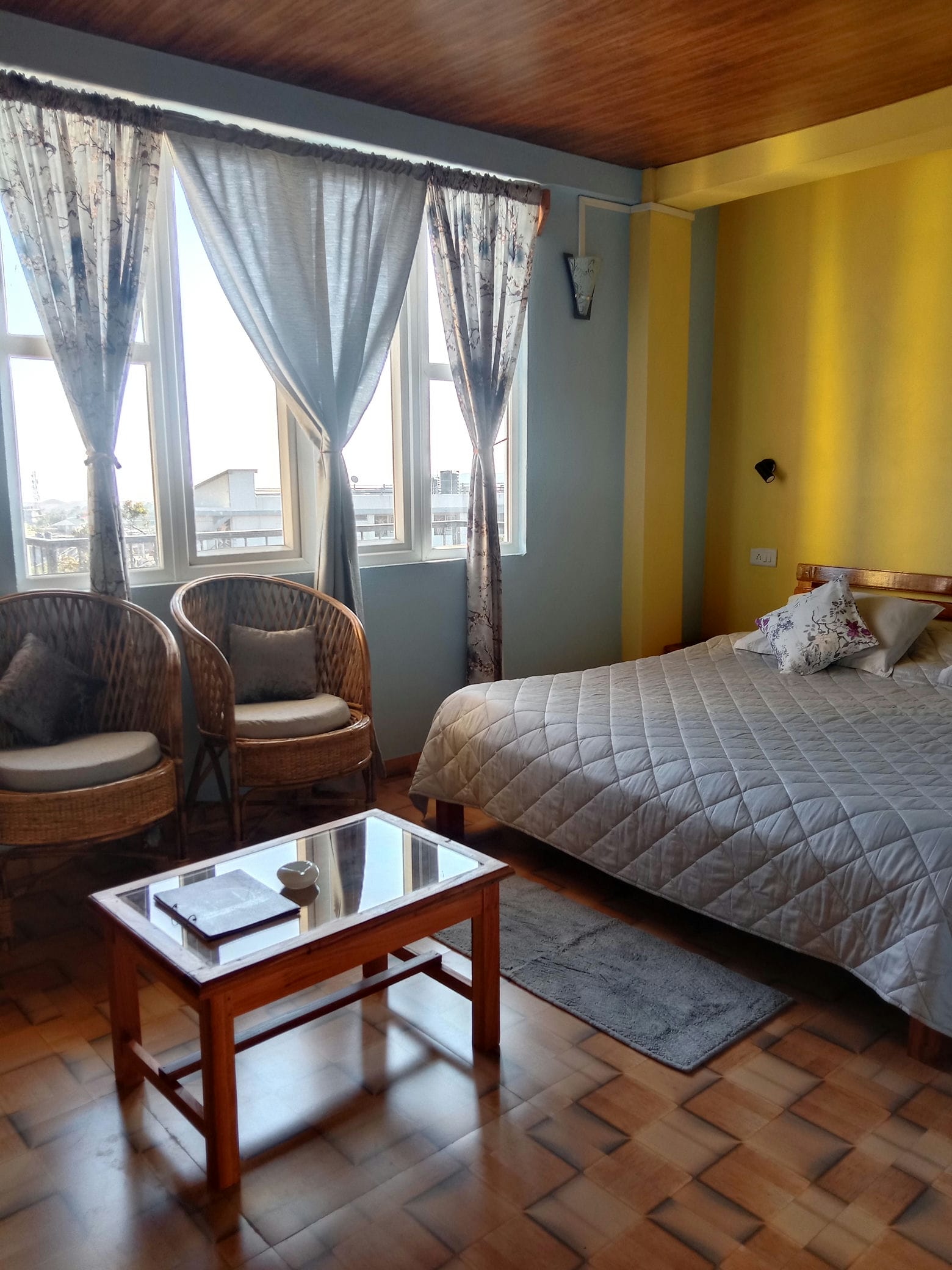 Accommodations present queen mattresses dressed in neat gray bedding alongside woven wicker lounge seats atop timber floors.