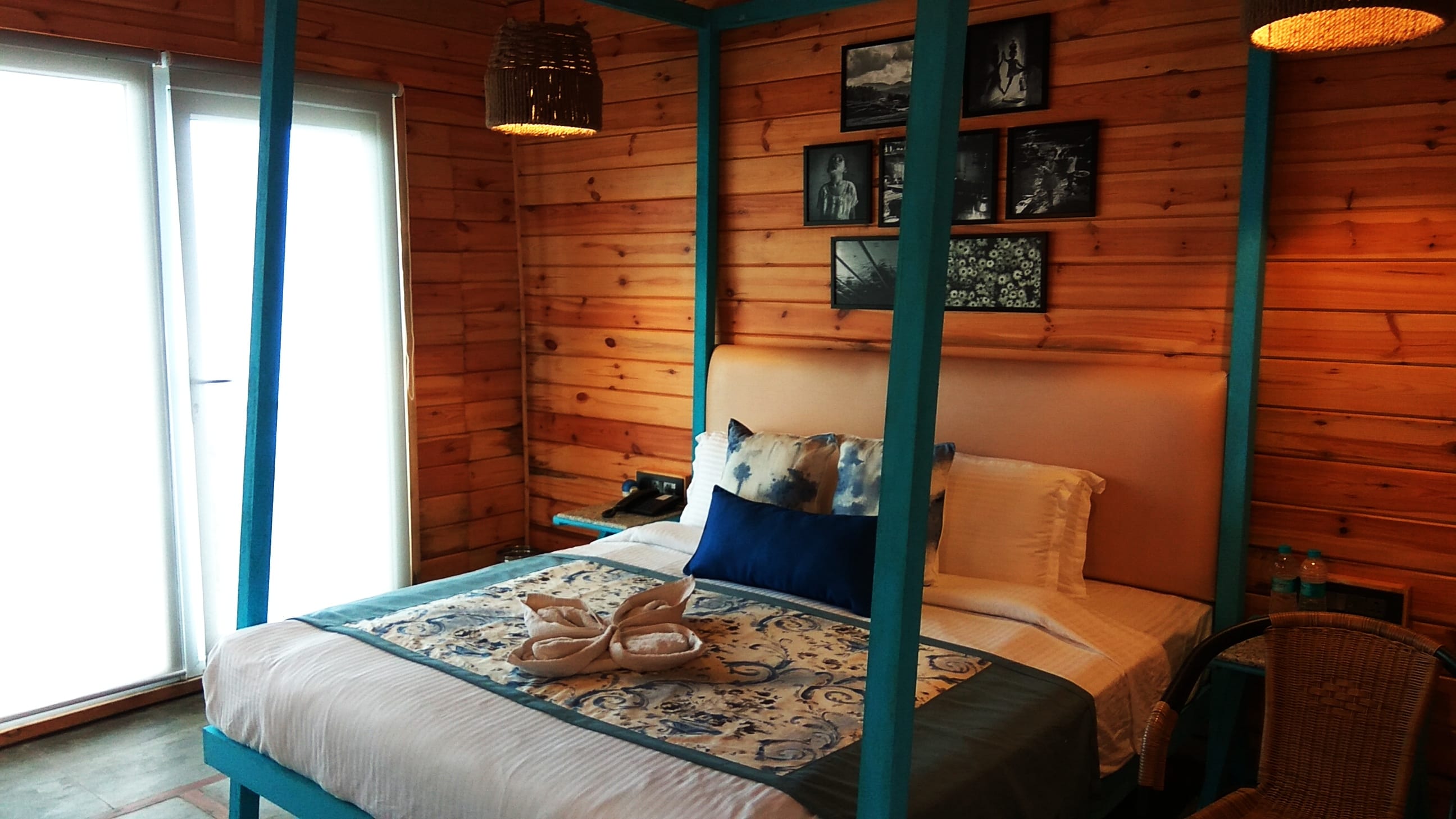 Classic Log Hut interior with vibrant teal 4-poster canopy bed and exposed timber beam ceiling.