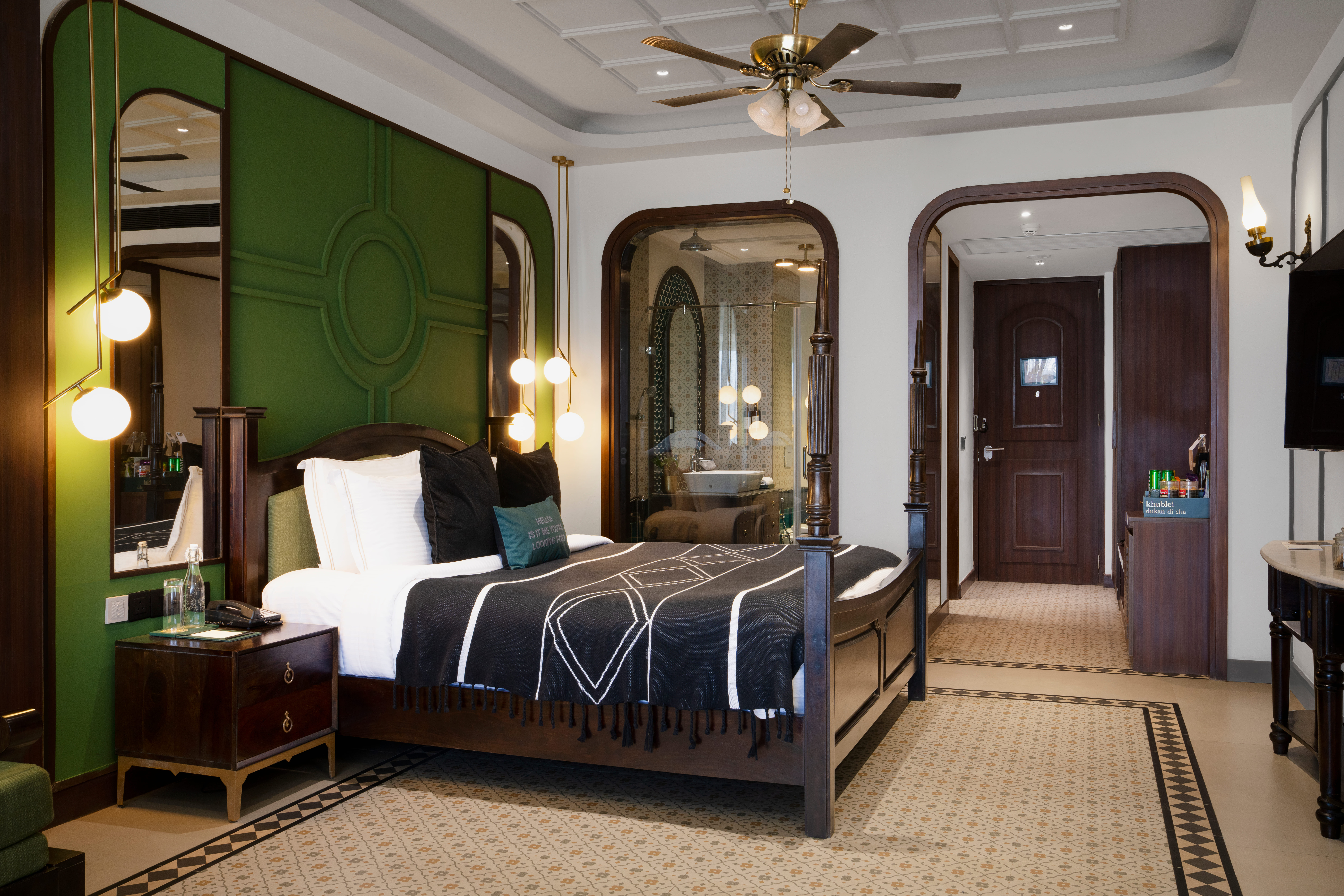 Elegant master bedroom in Sohra Family Suite featuring dark green feature wall and brass lighting.
