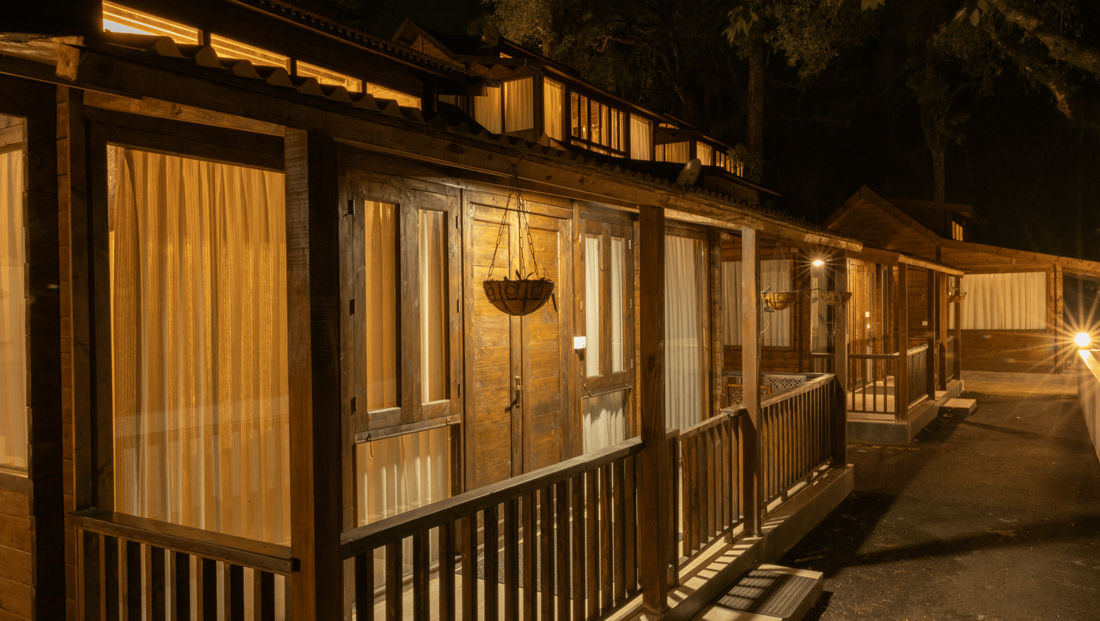 Covered timber veranda of the Forest Cottage at night decorated with hanging planters and warm exterior lights.