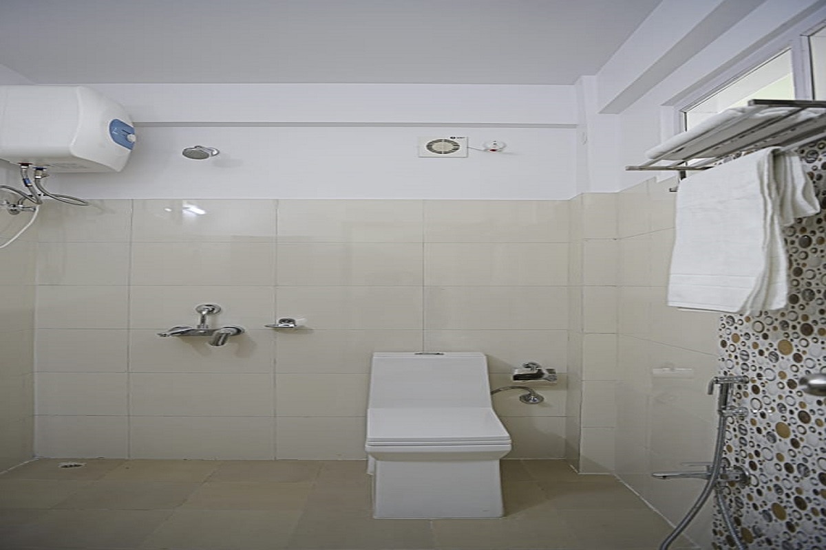 Clean tiled bathroom equipped with instant geyser water heater and towel rack.