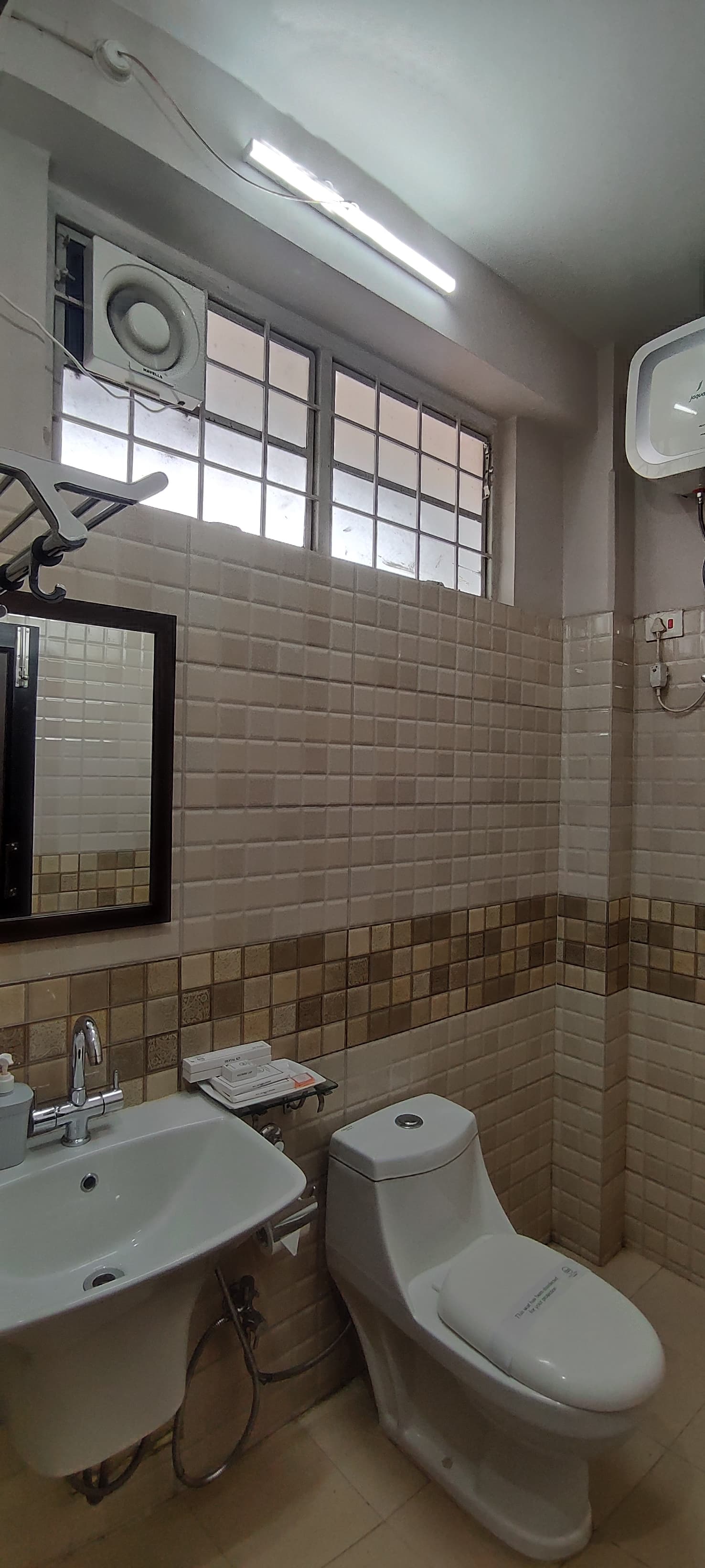Modern ensuite bathroom featuring ceramic wall tiles, chrome sink fixtures, vanity mirror, and ceiling exhaust fan.