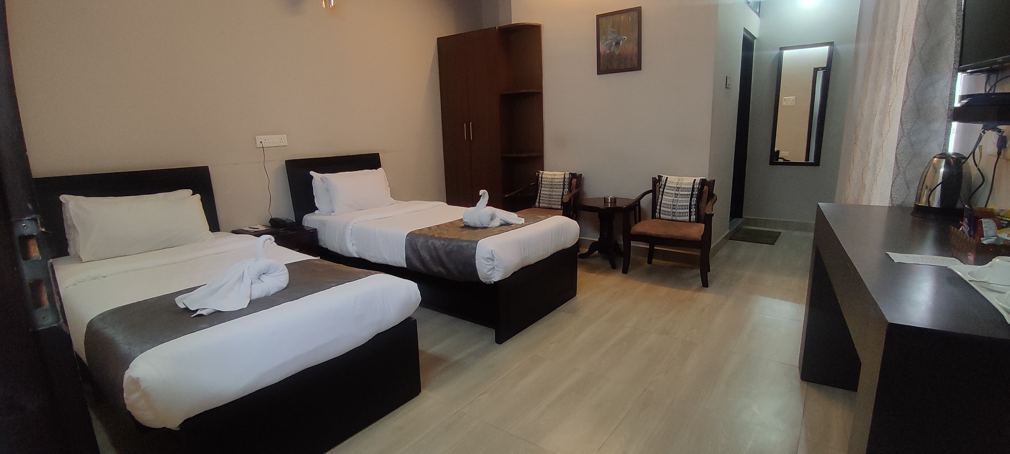 Standard Room furnished with twin single beds, a wooden wardrobe closet, and a pair of armchairs with coffee table.