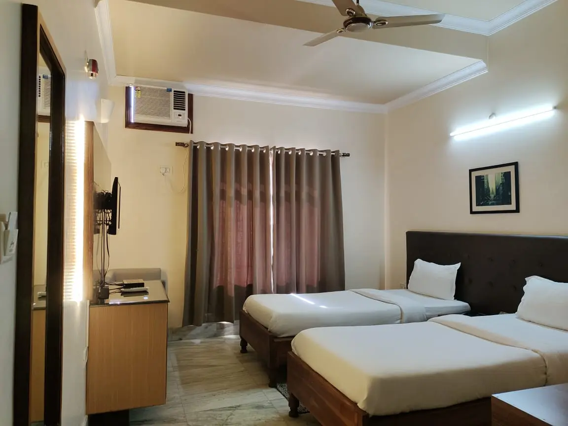 Configured for twin occupancy, this air-conditioned room features two single beds, individual window AC unit, ceiling fan, and large vanity mirror.