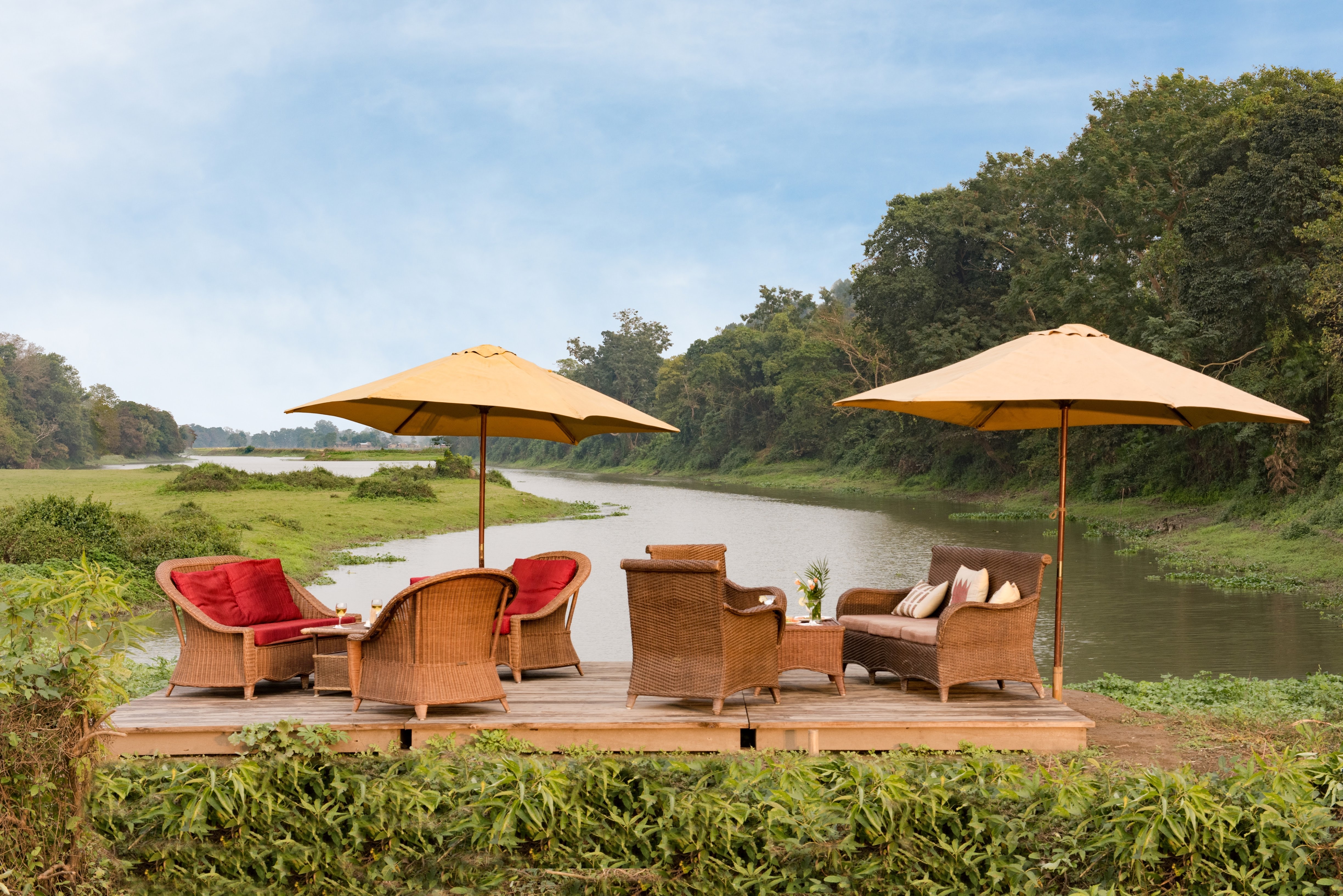 Riverfront viewing deck with cane armchairs and sun parasols overlooking the serene Diphlu River.