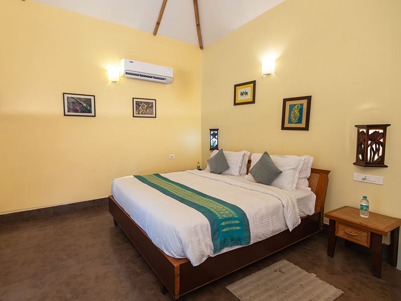 Master bedroom inside Bansbari Villa featuring king bed with traditional runner, bamboo rafters, and split air conditioner.