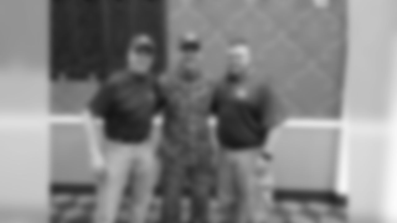 Pepper Burress and Tom Bakken posing for a picture with Gen. Charles Hudson who is wearing a USS Green Bay hat.