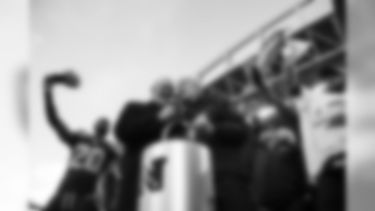 Head coach Pete Carroll accepts the Halas trophy from Terry Bradshaw on the podium as the team celebrates around him.