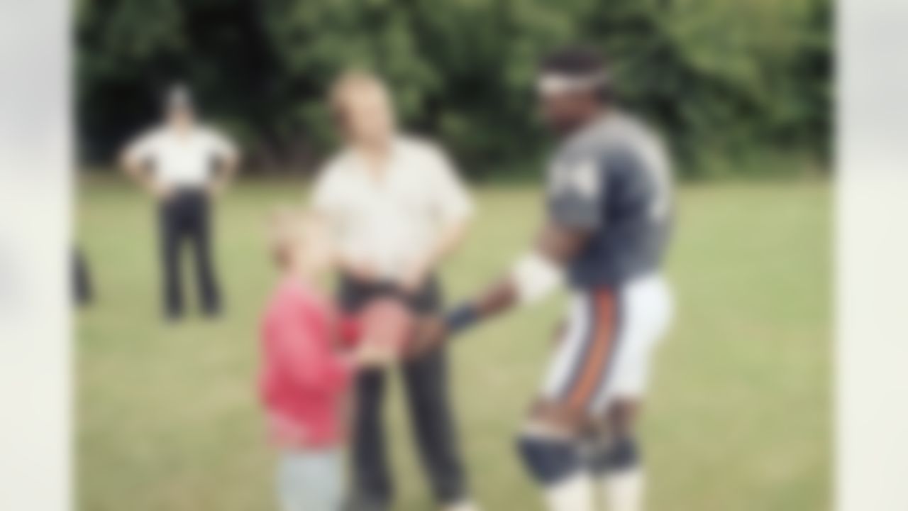 Pop Singer Phil Collins gets an autograph from Chicago Bears running back Walter Payton with his son, Simon, during a Bears workout in London on Friday, August 1, 1986. (Charles Bennett/Associated Press)