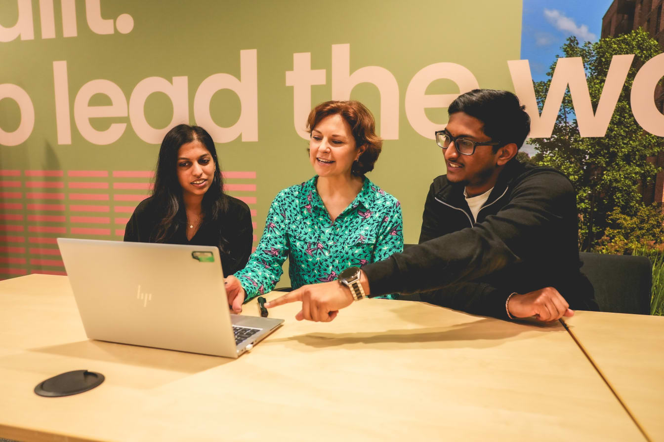 Three individuals gathered round a laptop, pointing and smiling