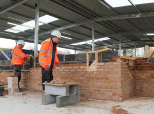 Kane and Kyle bricklaying at the training hub in orange safety clothing.