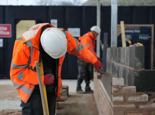 A man in wearing safety clothes and building a brick wall