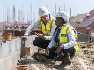 two people on site crouching while wearing site safety clothing and hard hats