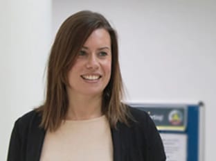 a woman in a black blazer smiling slightly off camera