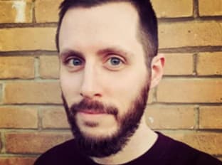 a man in a black shirt with a beard smiling at the camera