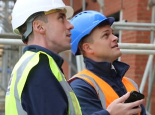 Two people in site safety clothing looking at some scaffolding on site