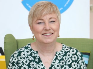 a woman with short blond hair in a blue and green shirt smiling at the camera
