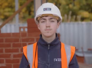 a young man in an orange high vis vest and white hard hat looking at the camera