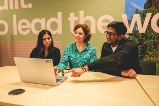 Three individuals gathered round a laptop, pointing and smiling