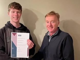 Two people smiling at the camera while holding an apprenticeship certificate