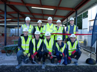 the bricklaying apprentice team in site safety clothing smiling at the camera