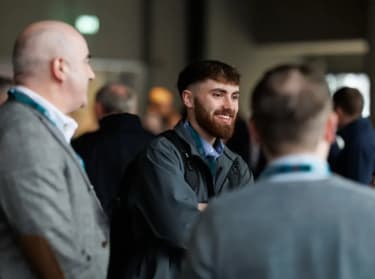 a man in grey suit standing in a crowd and smiling