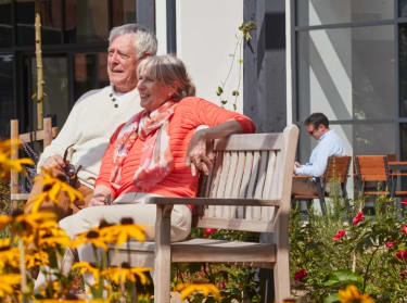 an older couple sitting on a bench in the sunshine
