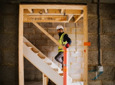 a man in high vis safety clothing walking up the stairs in an unfinished new build property.