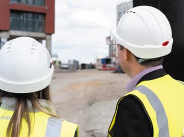 a man and a woman in site safety clothing and hard hat looking at a site