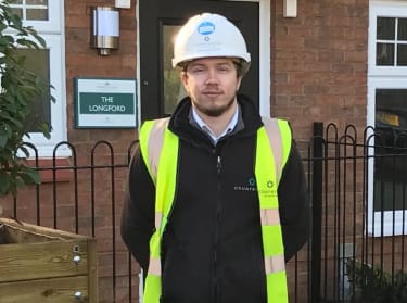 a man in site safety clothing and a hard hat on site smiling at the camera