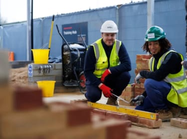A tutor and bricklaying apprentice smiling at the camera