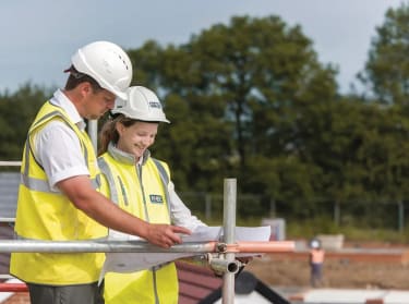 a man and a woman looking at construction drawings on a construction site