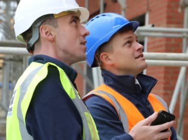 Two people in site safety clothing looking at some scaffolding on site
