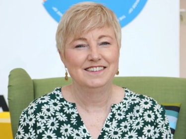 a woman with short blond hair in a blue and green shirt smiling at the camera