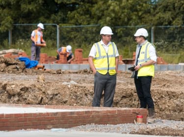 two men in site safety clothing and hard hats inspecting foundations on a site
