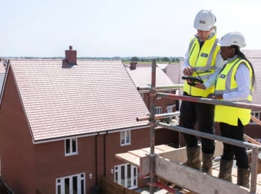 two people stood on scaffolding on site wearing site safety clothing looking at a tablet