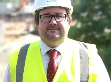 a man in a shirt and tie and site safety clothing smiling at the camera