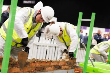 Two people in PPE laying bricks in the BEYOND '25 LIVE bricklaying competition