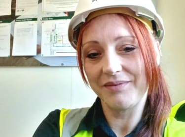 a woman in site safety clothing and a hard hat smiling at the camera