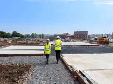 two people in high vis safety clothing walking on an unfinished new build site