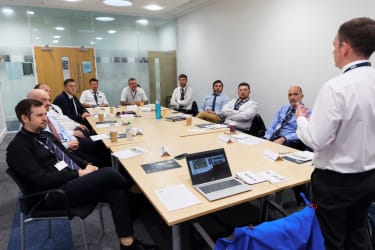 man teaching a group of people sat around a long table in a meeting room