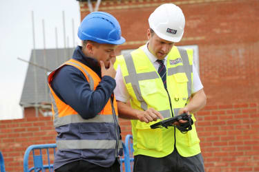 two men in site safety clothing and hard hats inspecting documents