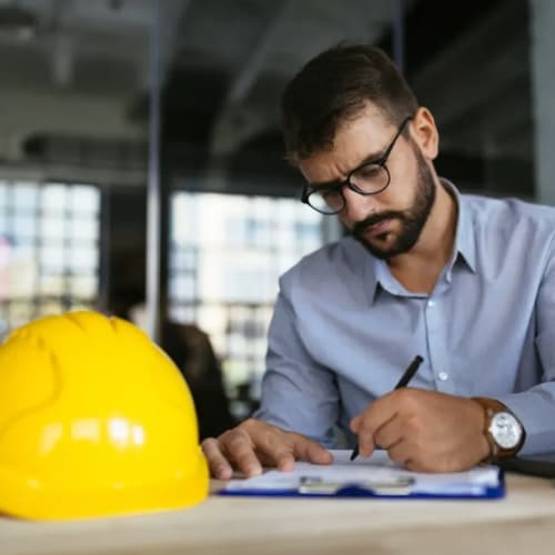 Man wearing glasses looking at report with hard hat on the table