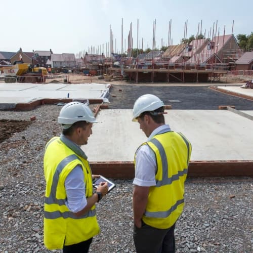 Two men wearing safety jackets and hard hats on new home development